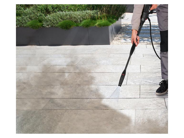 Personne nettoyant une terrasse avec un nettoyeur haute pression, enlevant la saleté des carreaux clairs.