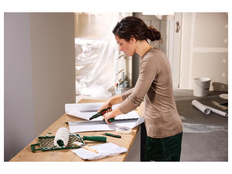 Femme coupant du papier peint avec un cutter, avec des fournitures de peinture sur la table.