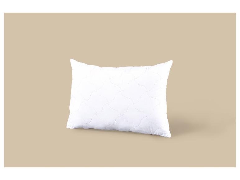 Oreiller blanc avec un motif de surpiqûres ondulées sur fond beige.