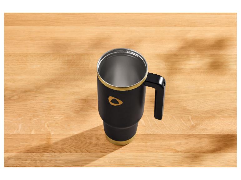 Mug thermique noir avec des accents dorés sur une table en bois.