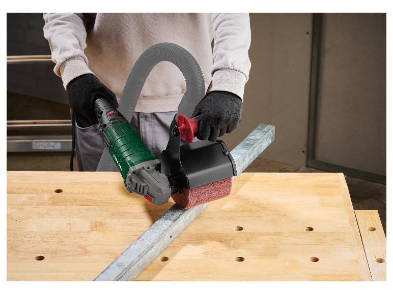 Personne utilisant un outil électrique avec une brosse pour nettoyer une poutre métallique sur un établi.
