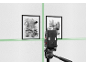 Niveau laser projetant des lignes vertes sur un mur blanc avec deux tableaux abstraits encadrés.