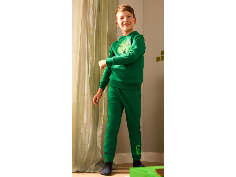 Garçon souriant en sweat à capuche vert et pantalon de jogging avec imprimé monstre.