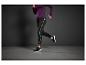 Une femme portant un legging noir avec des accents blancs et des baskets noires en courant.
