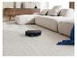 Robot aspirateur noir sur tapis clair avec canapé modulaire et buffet en bois.