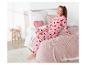 Une fille en pyjama rose avec des cœurs rouges est assise sur un lit avec une couverture rose.