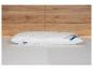 Un oreiller blanc matelassé avec des étiquettes de marque sur un lit, avec un mur en bois.