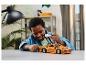 Un garçon souriant assemble une voiture de sport orange LEGO Technic sur une table.