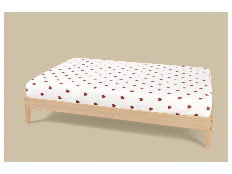 Drap blanc à cœurs rouges sur un cadre de lit en bois clair.