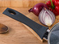Une casserole avec une poignée noire, un oignon rouge et un poivron rouge sur une planche à découper en bois.