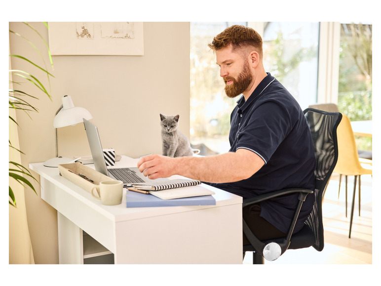 Un homme assis à un bureau avec un ordinateur portable, un cahier et une tasse de café.