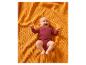 Un bébé souriant en body rouge est allongé sur une couverture orange texturée.