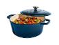 Cocotte en fonte bleue remplie de légumes colorés et d'herbes, avec le couvercle entrouvert.