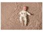 Un bébé dans une tenue blanche à imprimé ours, allongé sur une couverture beige.