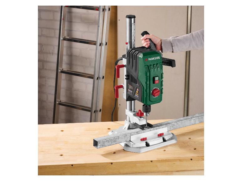 Une personne utilise une perceuse à colonne Parkside pour percer une barre métallique sur un établi.