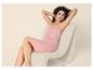 Femme aux cheveux bouclés se relaxant sur une chaise, vêtue d'une nuisette rose.