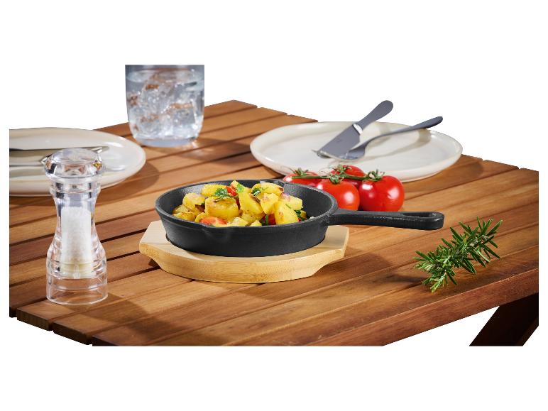 Poêle en fonte avec pommes de terre sautées, sel, tomates et romarin sur une table en bois.
