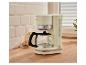 Cafetière filtre crème avec carafe, lait et biscuits sur un comptoir en bois.