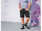 Un garçon porte un t-shirt gris, un short en jean noir et des baskets noires.