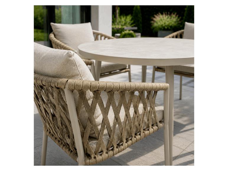 Ensemble de salle à manger d'extérieur avec table ronde et chaises tressées avec coussins clairs sur une terrasse.