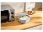 Micro-ondes gris avec un récipient en silicone de riz et une salade sur un comptoir en bois.