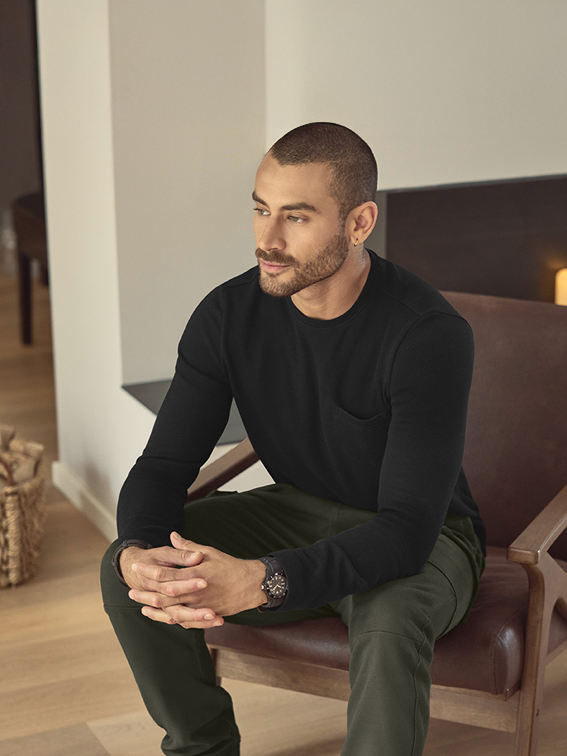 Homme en t-shirt noir à manches longues et pantalon vert, assis sur une chaise en cuir
