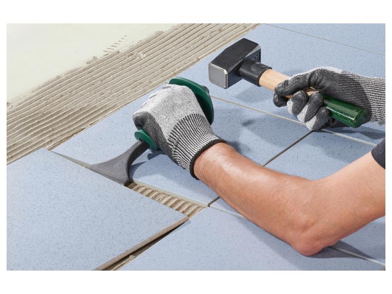 Homme posant des carreaux de sol avec un marteau et un outil de pose.