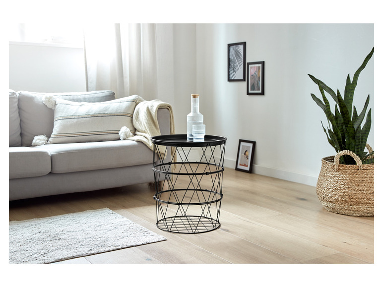 Une table basse en métal noir avec un vase en verre et une plante dans un panier en osier.
