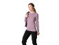Femme en t-shirt à manches longues mauve et pantalon noir, avec un sac à dos sur l'épaule.