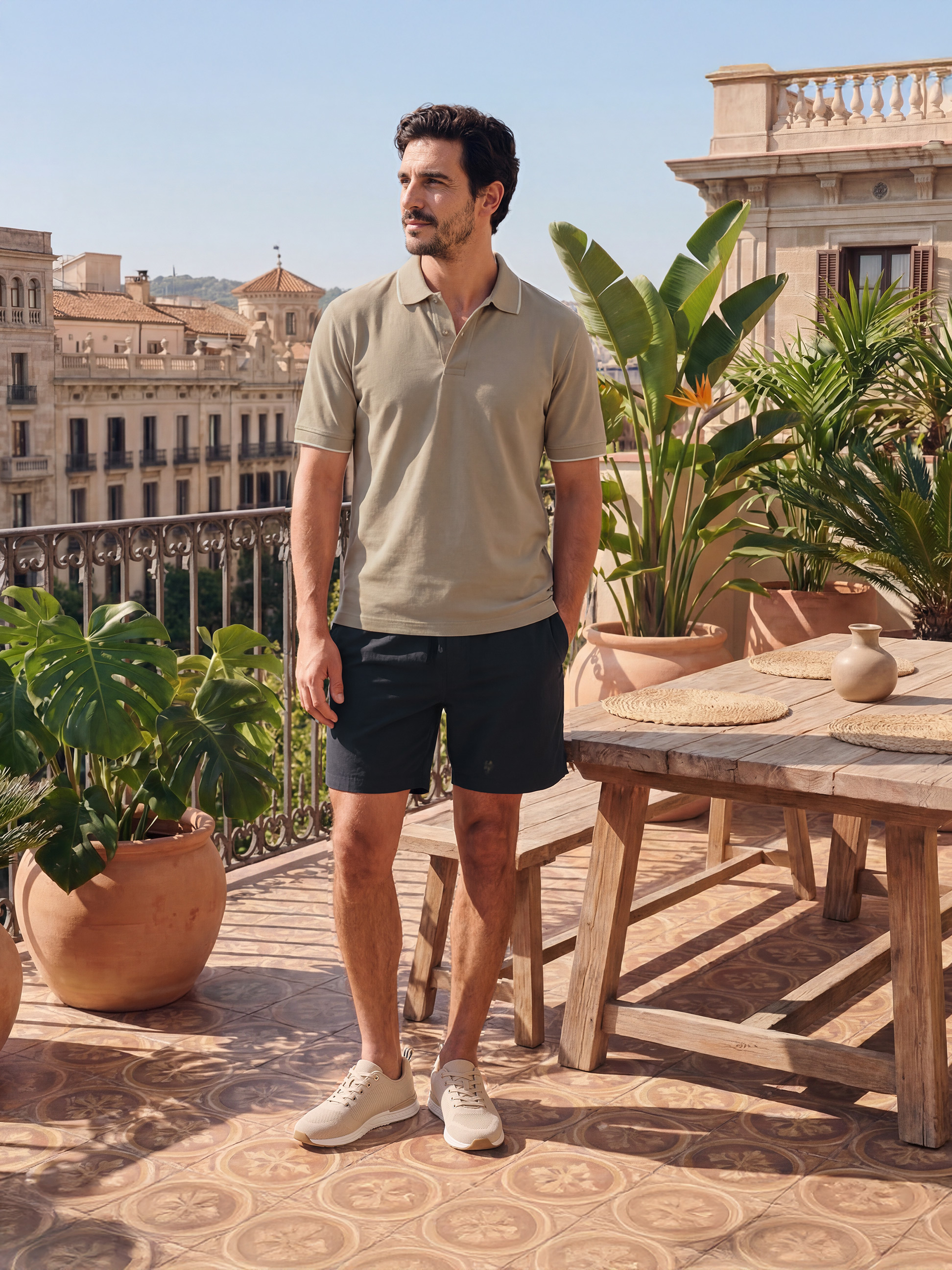 Homme en polo beige et short noir sur une terrasse ensoleillée avec vue sur la ville.