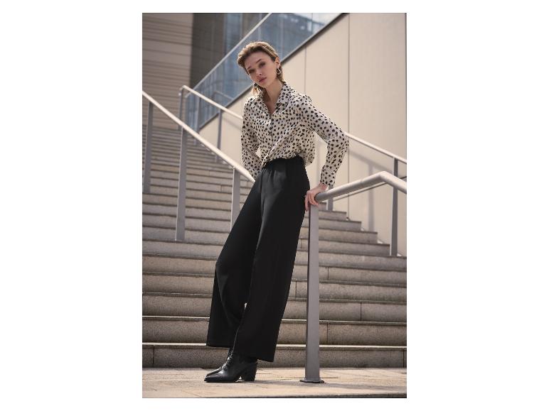 Femme en chemise imprimé léopard et pantalon noir, appuyée sur une rampe.