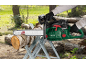 Tronçonneuse à batterie verte coupant une bûche de bois sur un tréteau en extérieur.