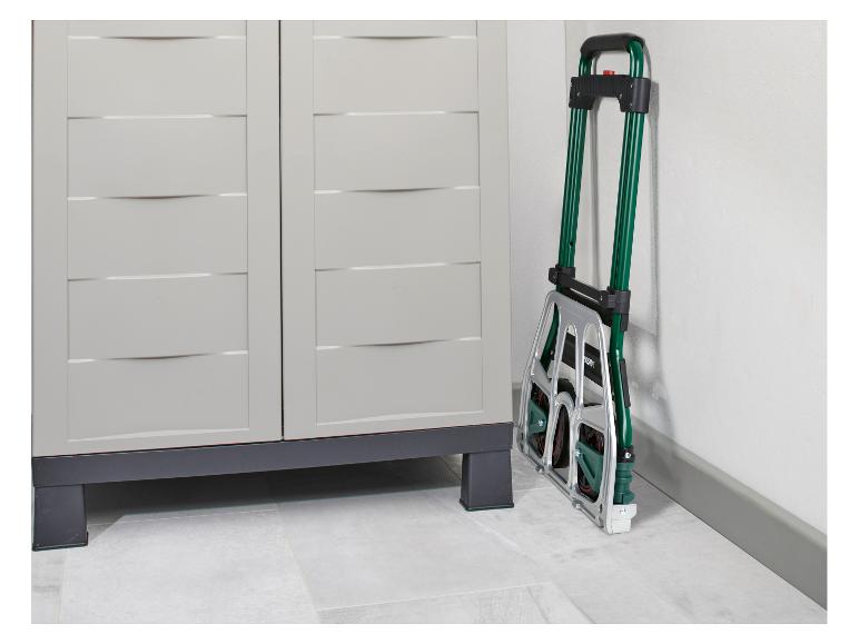 Un diable pliant vert et argenté appuyé contre un mur blanc à côté d'une armoire de rangement gris clair.