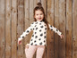 Une petite fille porte un t-shirt rose avec des pommes noires et un pantalon rose à pois blancs.