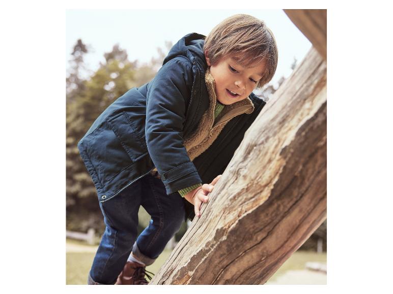 Garçon en veste marine et jean, grimpant sur un tronc d'arbre.