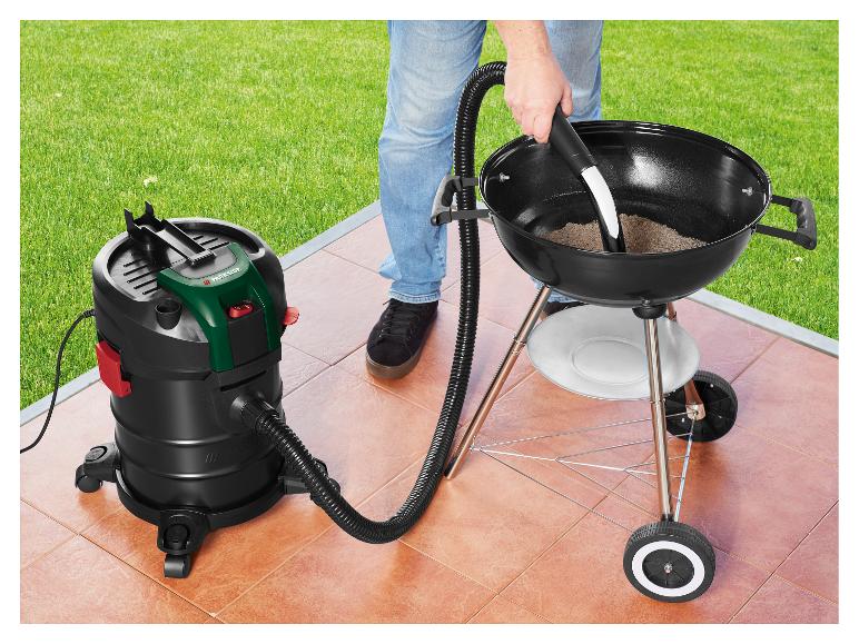 Aspirateur à cendres nettoyant un barbecue sur une terrasse, avec pelouse verte en arrière-plan.