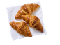 Trois croissants dorés sur une serviette blanche, vue de dessus.