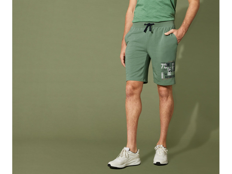 Un homme portant un short vert avec l'inscription 'United Club' et des baskets blanches.