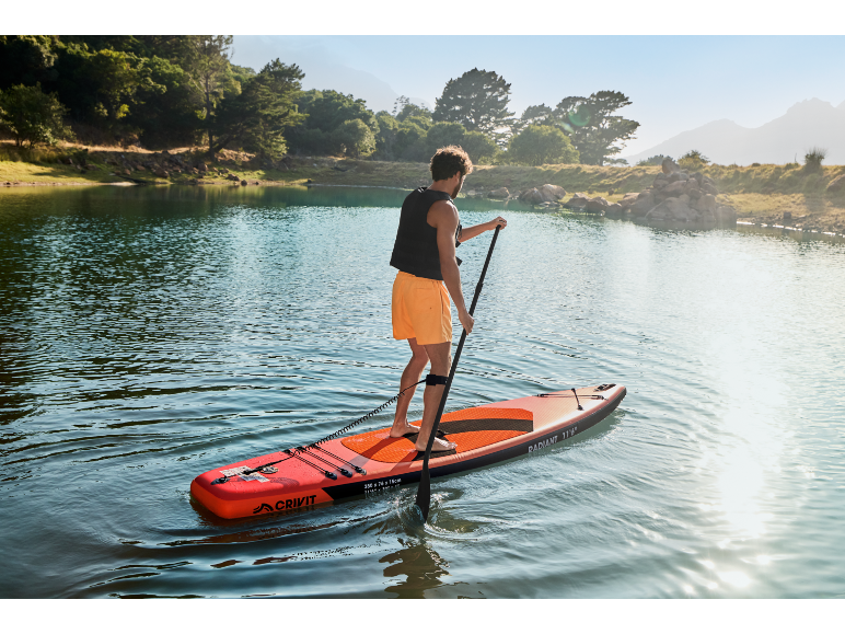 Homme faisant du paddleboard sur un lac, entouré d'arbres et de montagnes.