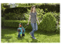 Une femme promène un dérouleur de tuyau d'arrosage Gardenena dans son jardin.