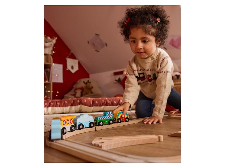 Un enfant joue avec un train en bois coloré sur un plancher en bois.