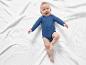 Un bébé dans un body bleu sur une couverture blanche.