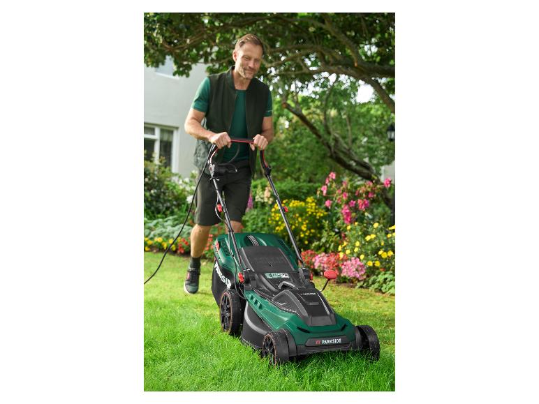 Homme tondant la pelouse avec une tondeuse à gazon électrique Parkside dans un jardin fleuri.