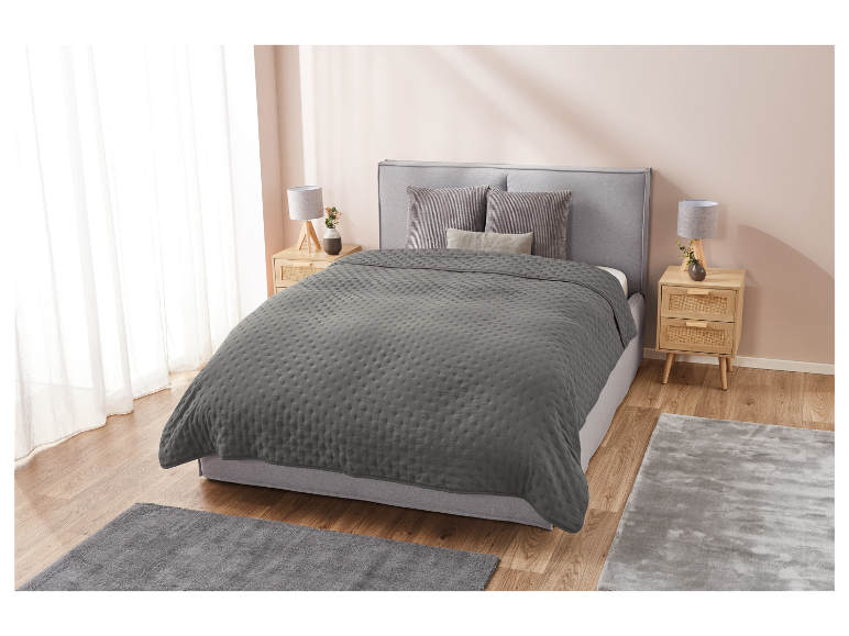 Une couverture grise matelassée sur un lit gris dans une chambre à coucher.