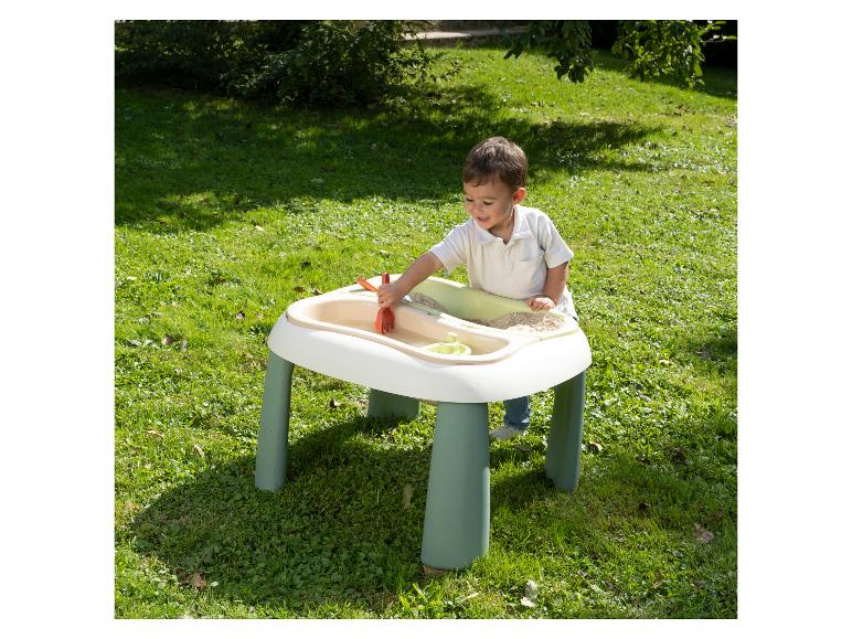 Jeune enfant jouant avec une table de sable et d'eau à l'extérieur sur l'herbe.