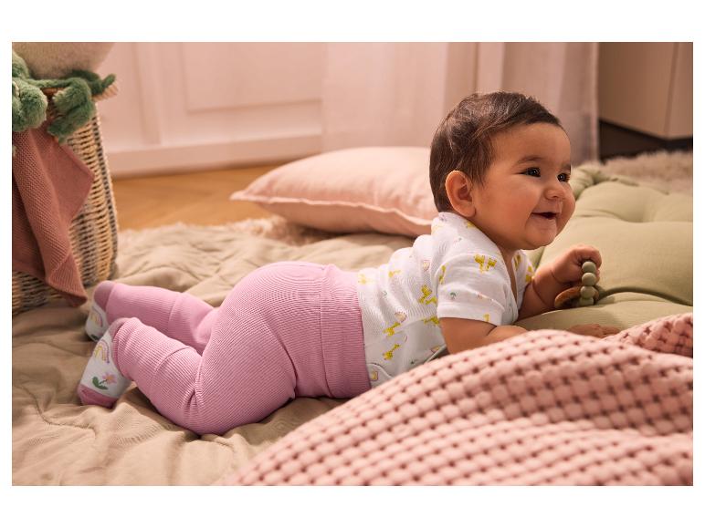 Bébé souriant en legging rose et body à motifs girafes, allongé sur le ventre.