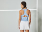 Une femme portant un débardeur bleu clair et une jupe de tennis blanche.