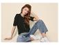 Femme en cardigan noir, jean ample et baskets blanches, assise sur le sol.