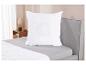 Oreiller blanc avec insert en mesh sur un lit gris.