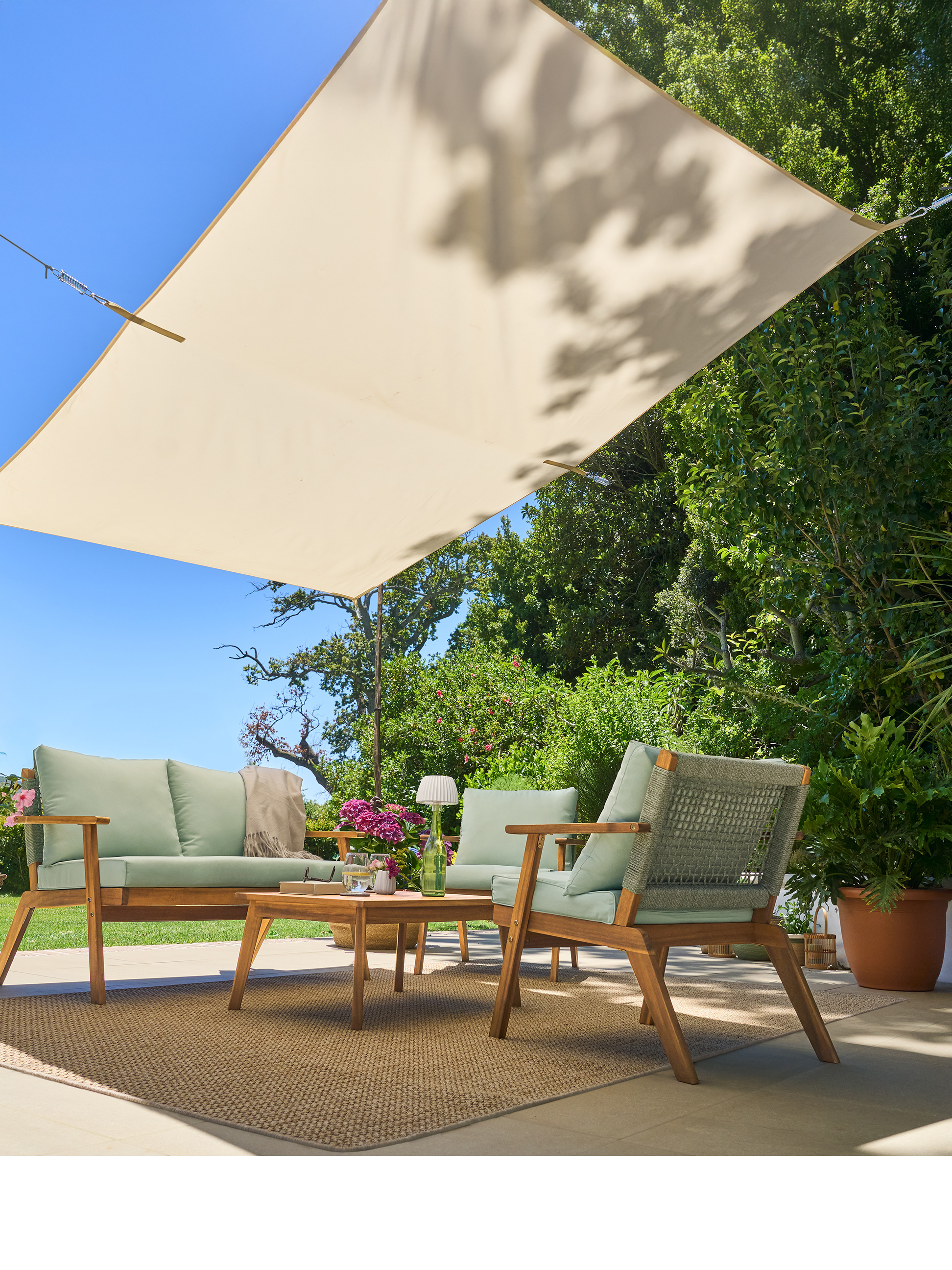 Ensemble canapé et fauteuils en bois avec coussins verts, table basse et voile d'ombrage sur un patio.